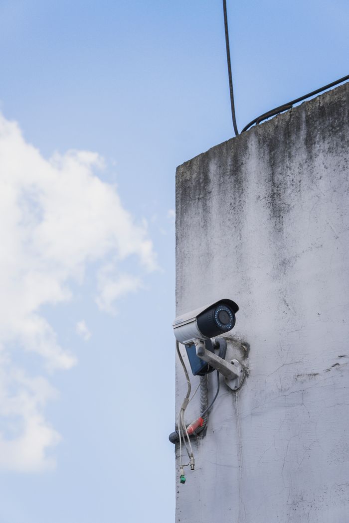 who-we-are Outdoor security camera attached to a weathered concrete wall under clear sky.