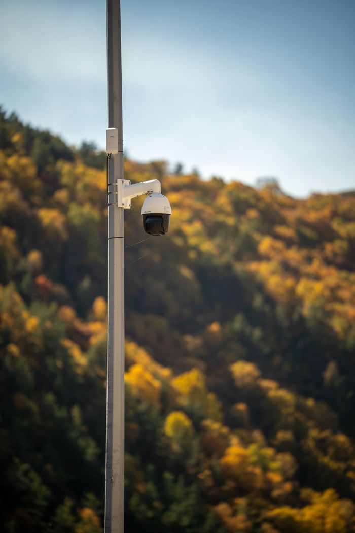 about-us CCTV camera on a pole with vibrant autumn foliage in the background, ensuring safety.