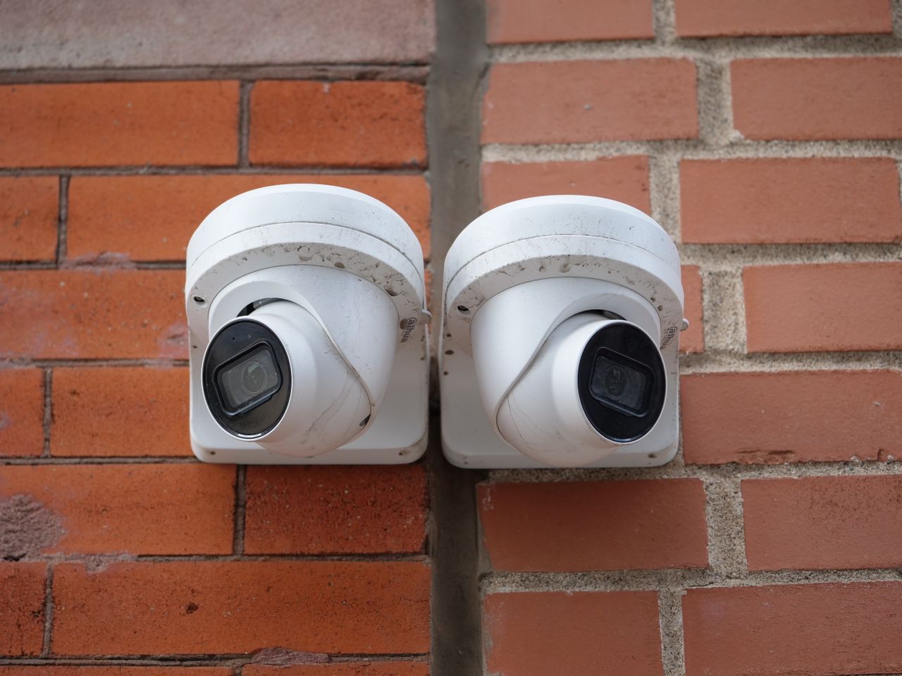 Two white dome security cameras mounted on a brick wall for urban surveillance.
