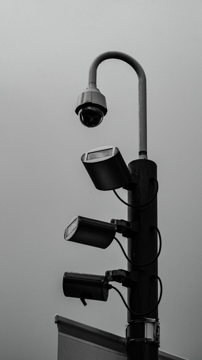 From below black and white of outdoor post with lamp and spotlights with multidirectional lighting pointing in four directions against sky