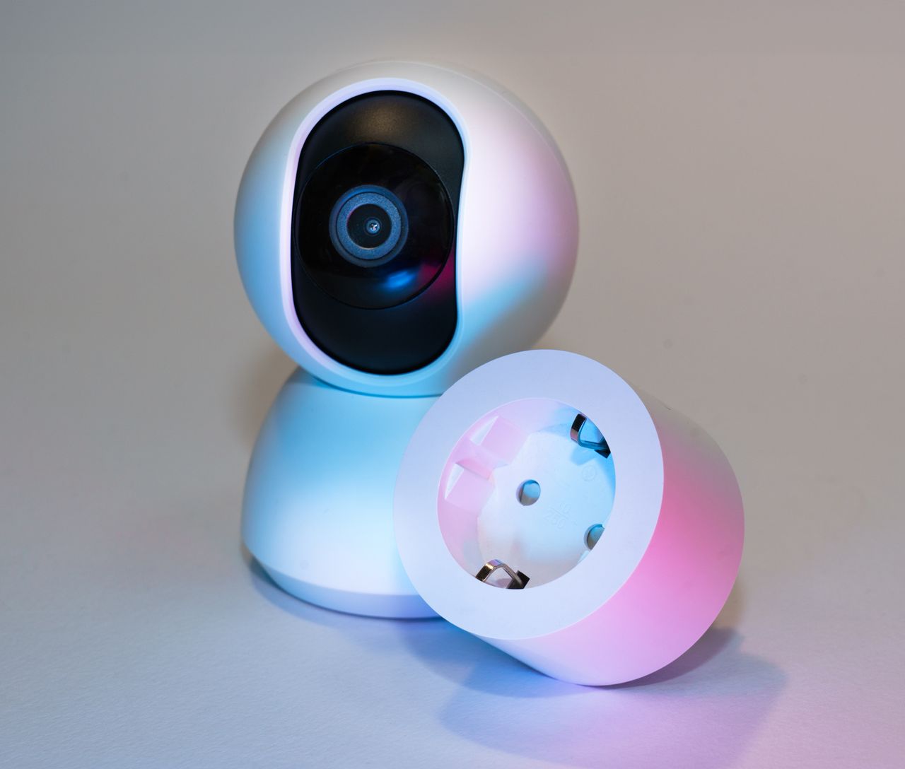 Smart home security camera and plug socket on a neutral background.